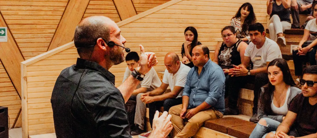Felipe Bozzo, con micrófono de cintillo, conversa con jóvenes y adultos sentados en las graderías de madera de un anfiteatro