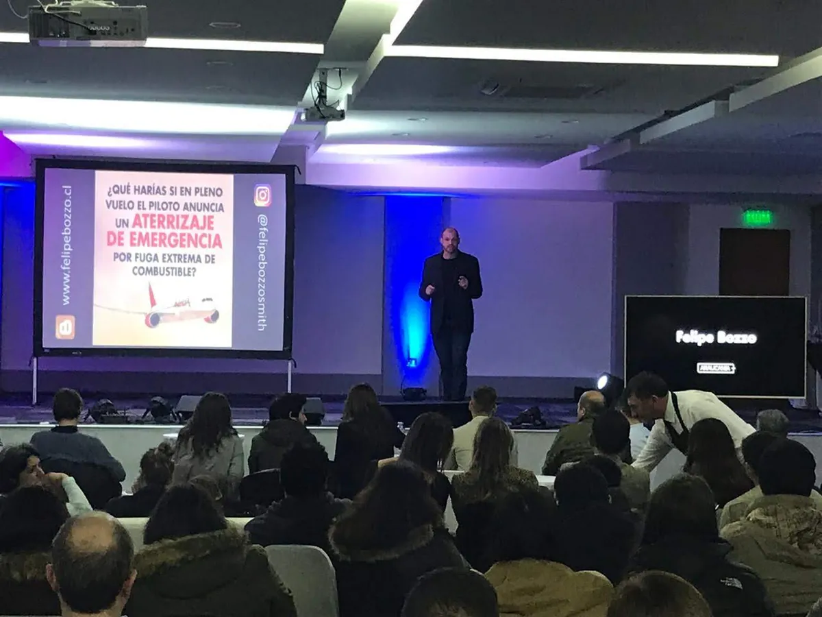 Felipe Bozzo en el escenario de un auditorio, ante el público, junto a la pantalla de una conferencia
