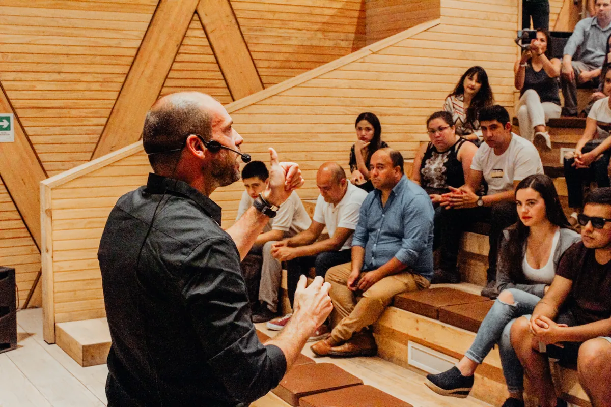 Felipe Bozzo, con micrófono de cintillo, conversa de cerca con un grupo de personas sentadas en las gradas de un anfiteatro de madera