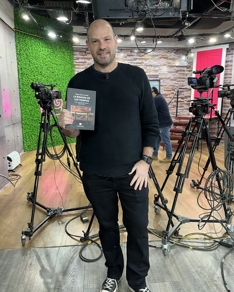 Felipe Bozzo muestra un ejemplar de «La Bisagra de los Tiempos» en un set de televisión, entre cámaras